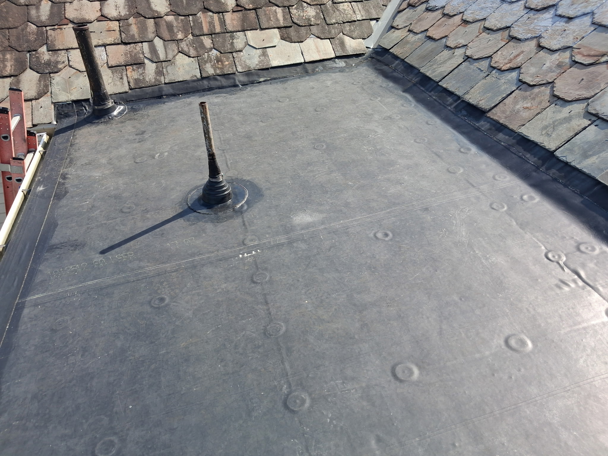 EPDM rubber roofing installation on a flat roof section with plumbing penetrations and watertight seal