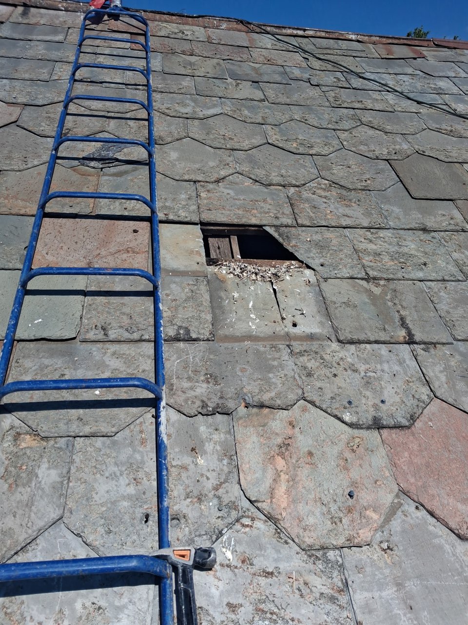 Before slate roof repair showing a missing slate section and exposed wood beneath the roof surface